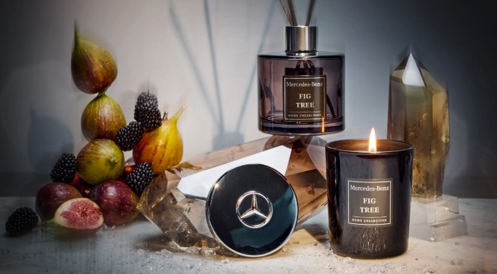 Dekoration mit Mercedes-Benz Duftkerze und Raumduft Fig Tree, daneben Kristalle, Feigen und Brombeeren auf heller Oberflaeche.